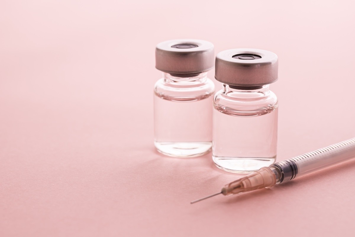 Syringe and vial on pink background.