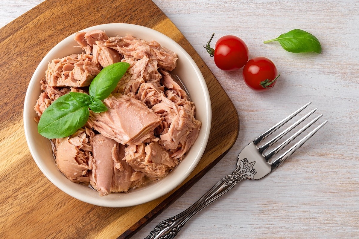 Can of tuna in a white bowl on a wooden cutting board.