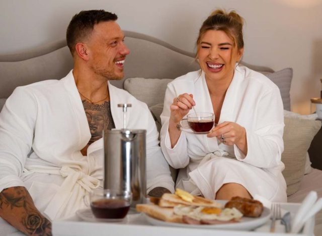 Olivia and Alex Bowen from 'Love Island' laughing while enjoying breakfast in bed at a hotel