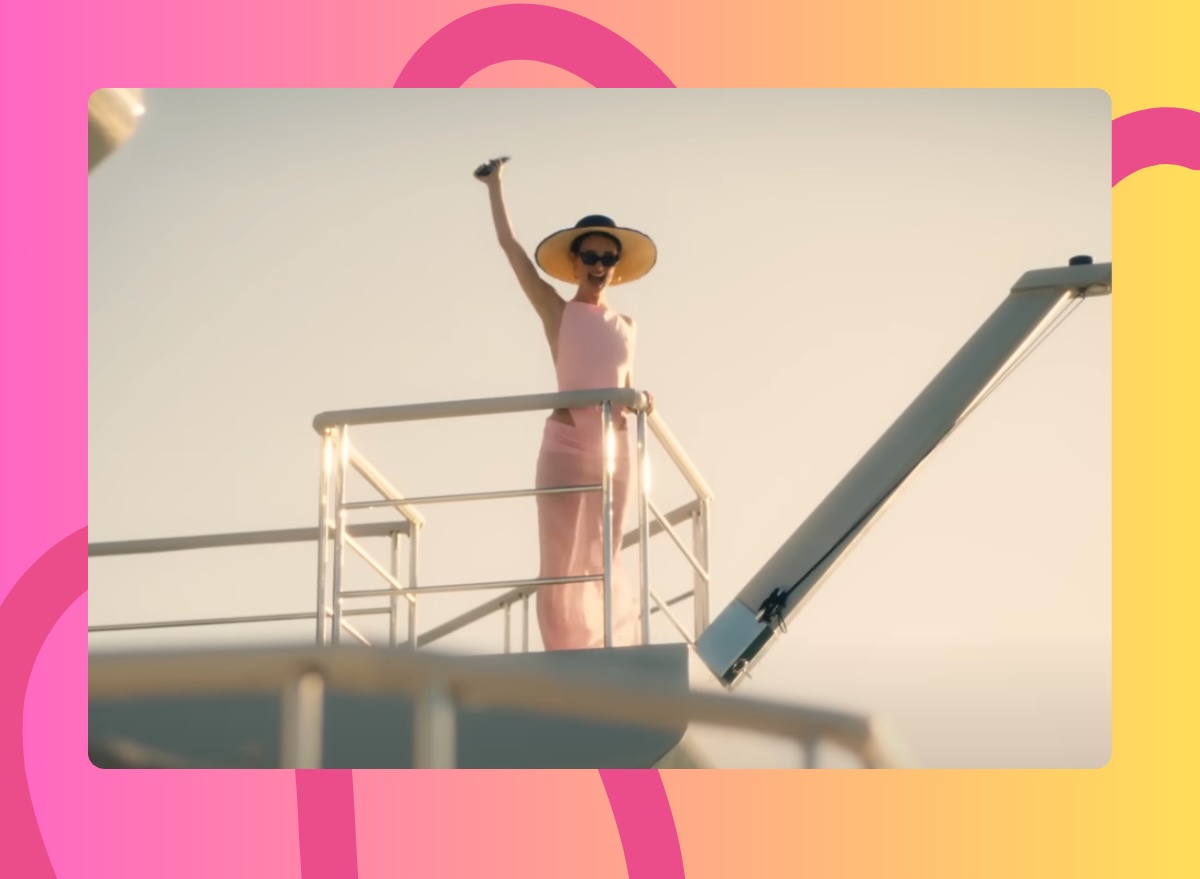 The White Lotus Chloe waving on a yacht in matching pink swimsuit and sarong